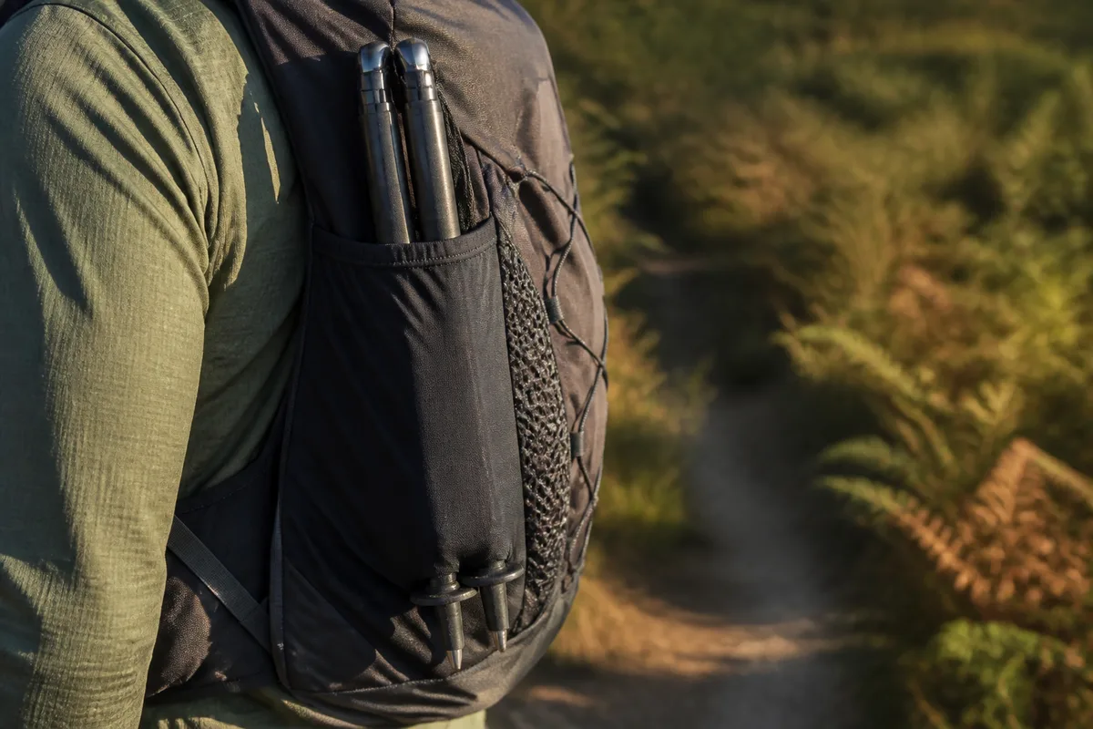 Bâtons pliants glissés dans le carquois latéral d’un sac de trail, pointes dirigées vers le bas