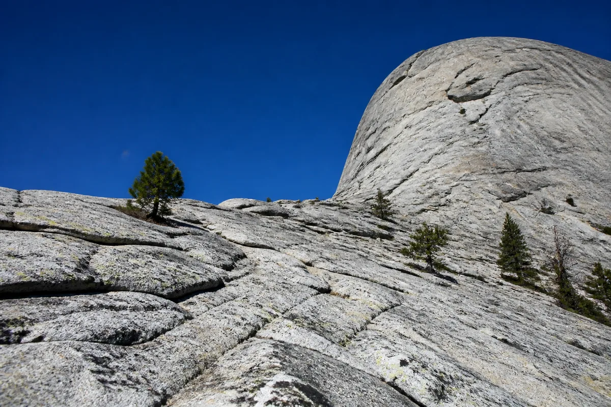 Dalle de granite claire montant vers un dôme rocheux, ciel bleu profond de fin de matinée