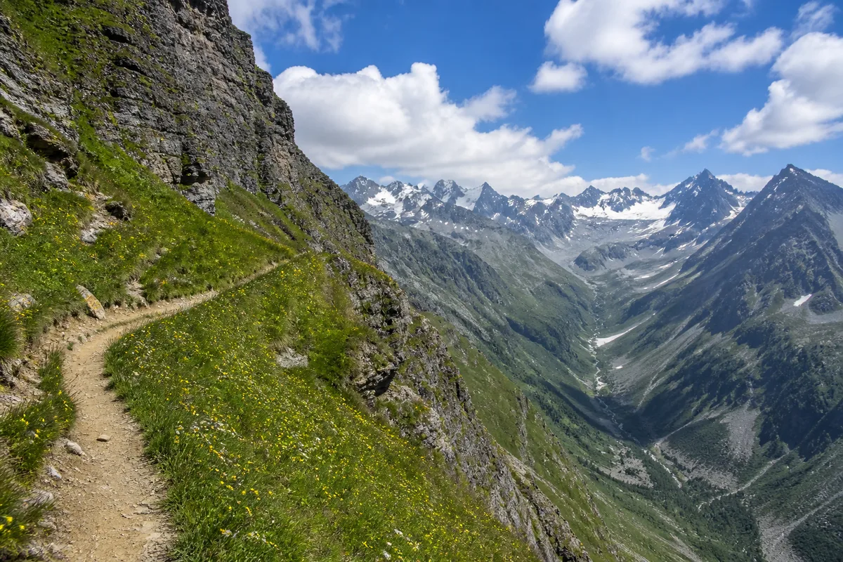 Vire herbeuse en balcon au-dessus d’une vallée glaciaire, névés résiduels et lumière claire de fin de matinée